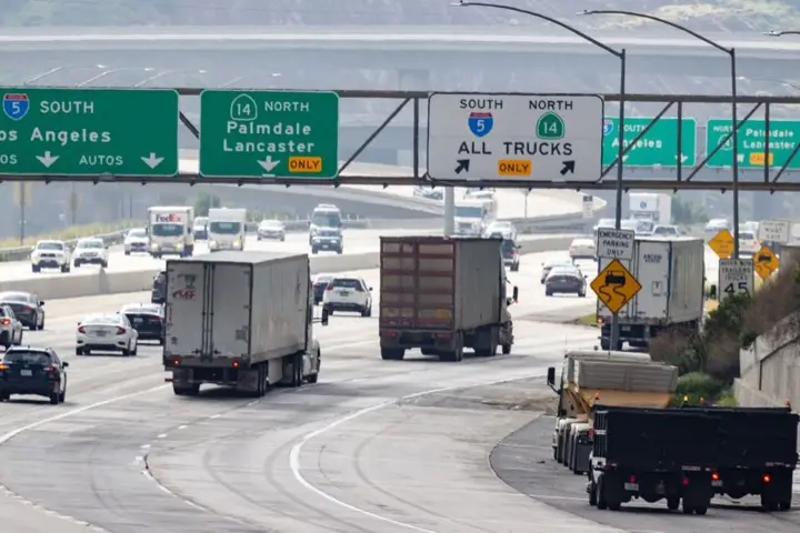 Trucks and cars under green freeway signs in the Los Angeles area