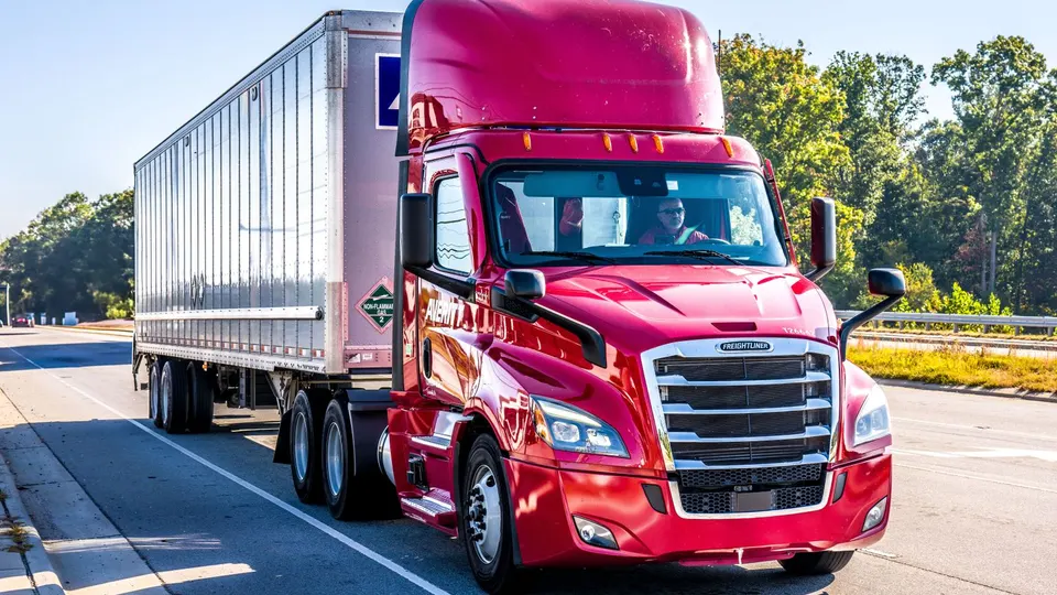 A red commercial truck pulling a trailer on a U.S. highway