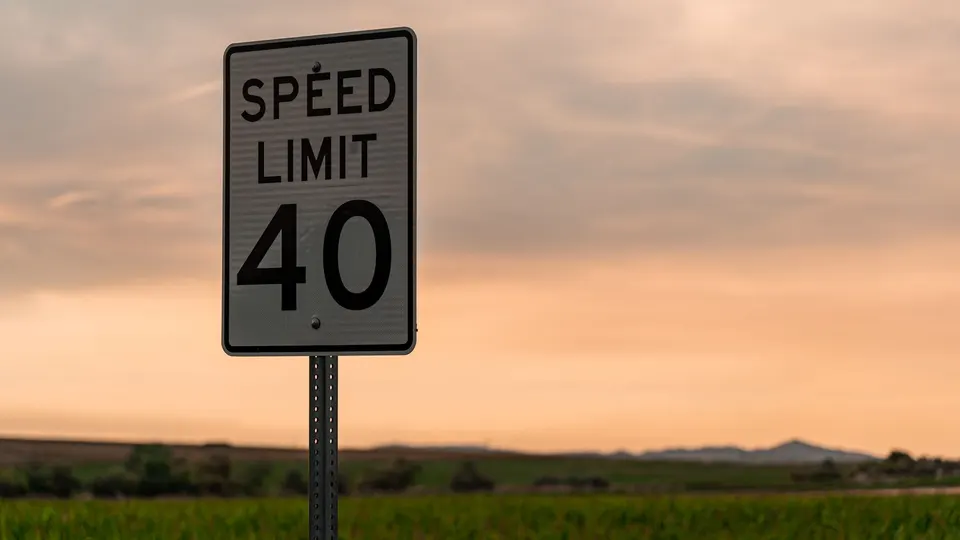 A black-and-white speed limit sign against an evening sky