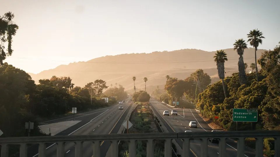 Cars on a Southern California freeway at sunset with palm trees and hills