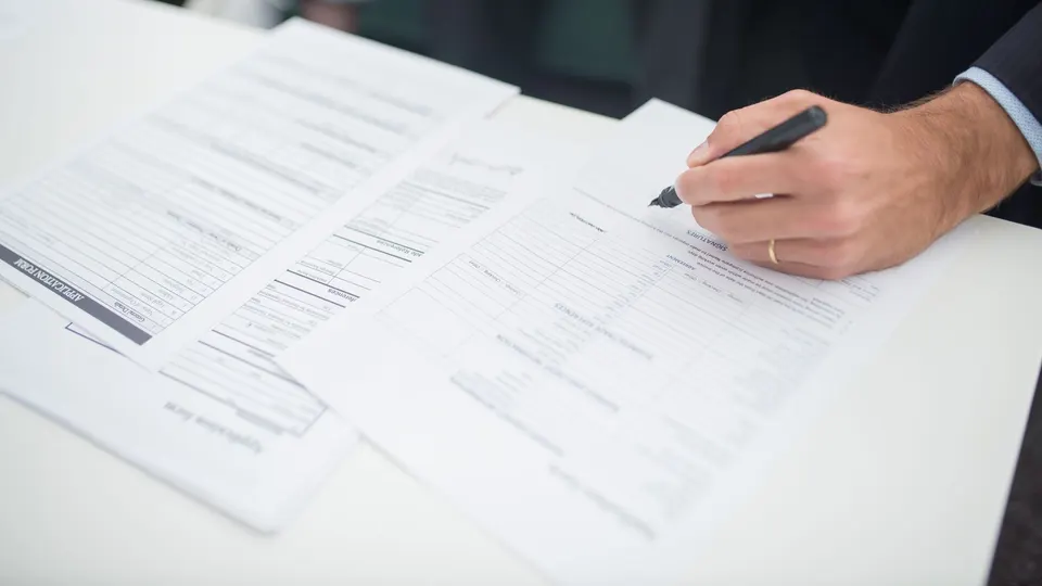 Hands filling in forms on a white desk