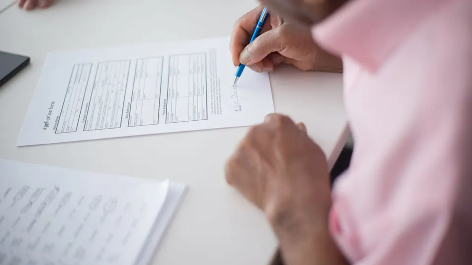 A person writing on a printed form with a pen