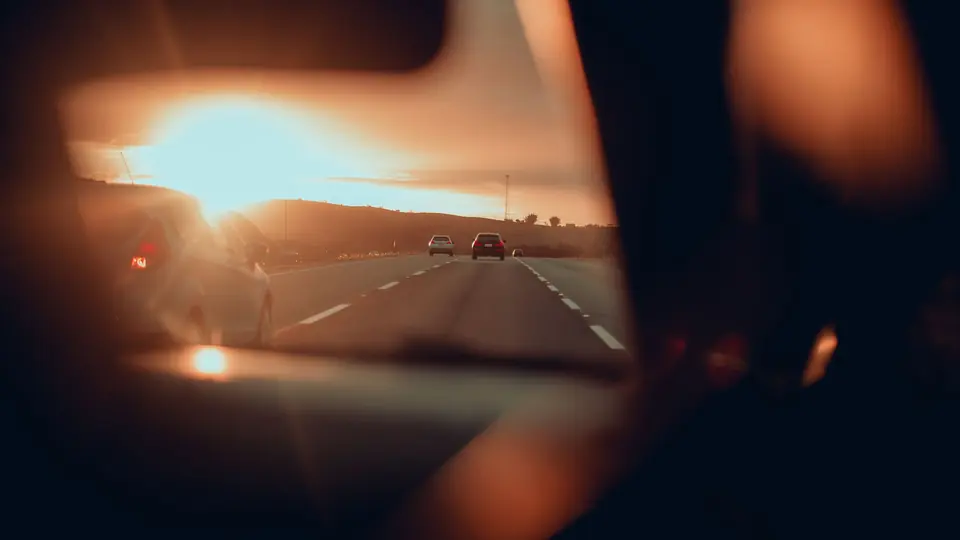 Cars on a road at sunset seen in a car's rearview mirror