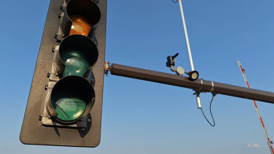 A traffic signal with a camera mounted on the pole above the intersection