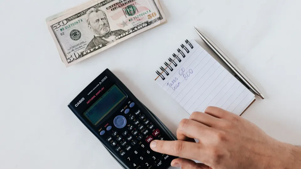 A calculator, a notebook and U.S. dollar bills on a white desk