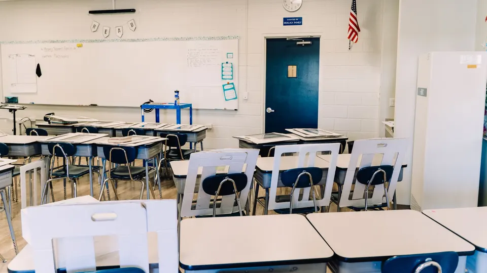 A bright classroom with desks, a whiteboard and a U.S. flag