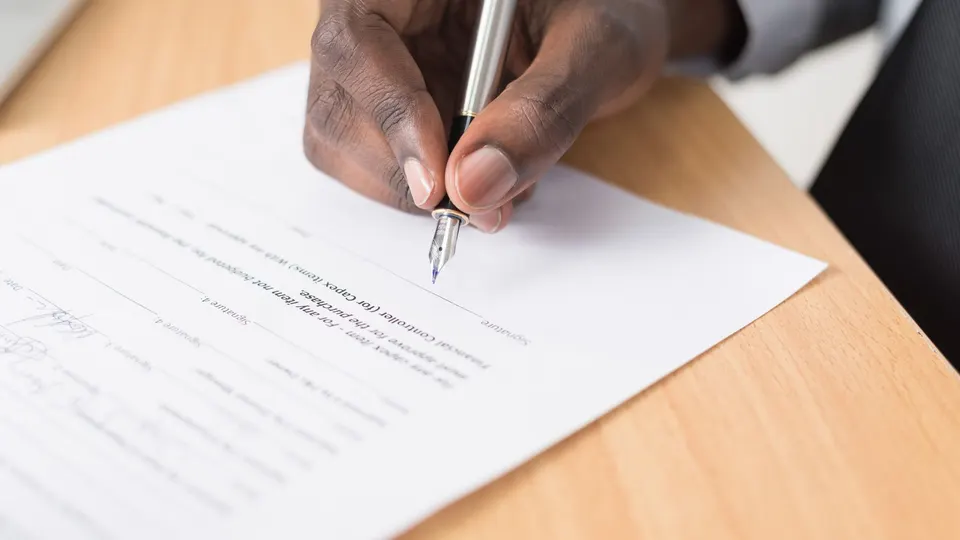 A hand signing a document with a pen